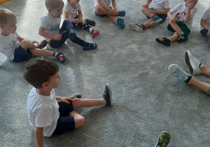 Dzieci siedzą na dywanie wykonując ćwiczenie.