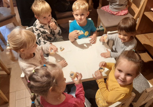 Dzieci siedzą przy stole i jedzą ciasteczka.
