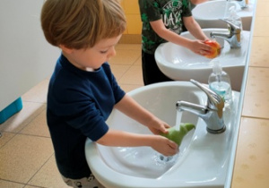 Troje dzieci myje owoce.