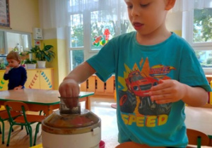 Chłopiec stoi przy stoliku- wkłada owoce do sokowirówki-szykuje dla siebie porcję soku.