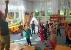 Dzieci stojąc na dywanie naśladują ruchy wykonane przez ciocię Kasię- unoszą ręce w górę.