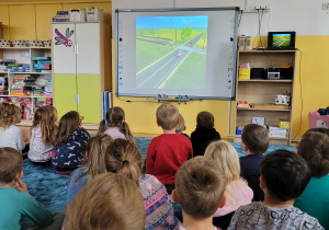 Dzieci oglądają film edukacyjny dotyczący bezpieczeństwa na przejeździe kolejowym.