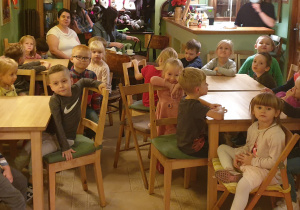 Dzieci siedzą przy stolikach i czekają na przedstawienie.