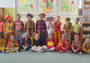 Dzieci siedzą na dywanie i prezentują swoje jesiene stroje.