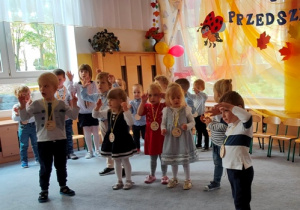 Dzieci stojąc w luźnej grupce na dywanie wspólnie śpiewają okolicznościową piosenkę ilustrując ją ruchem.
