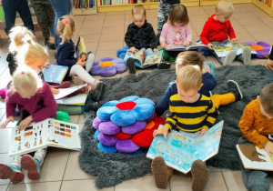 Dzieci siedzą na poduszkach w luźnej grupie- oglądają książki dla dzieci.