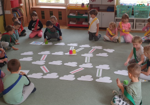 Dzieci podzielone na cztery grupy grają na dywanie w grę planszową.