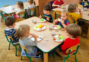Dzieci jedzą z apetytem śniadanie, jedno dziecko obserwuje rówieśników.