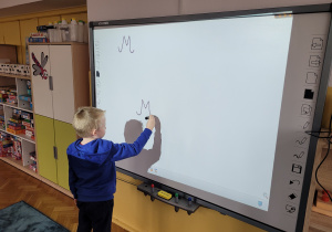 Tymon zapisuje na tablicy interaktywnej literę "M,m".