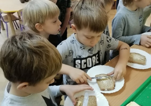 Chłopcy smarują masłem kromki chleba.