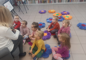 Dzieci siedzą na kolorowych poduszkach i słuchają opowiadania.