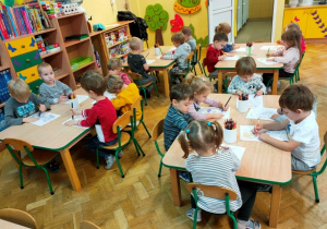 Dzieci siedzą przy stolikach, kolorują obrazki kredkami ołówkowymi.