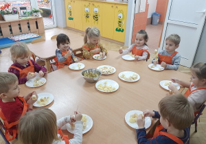 Dzieci siedząc przy stole robią szaszłyki owocowe.