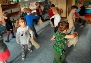 Dzieci stoją na dywanie w rozsypce. W rytm muzyki tańczą z chusteczkami trzymanymi w ręku.