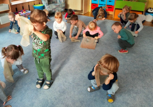 Dzieci na przerwę w muzyce kucają na dywanie , układają chusteczkę w wybrany przez siebie sposób.