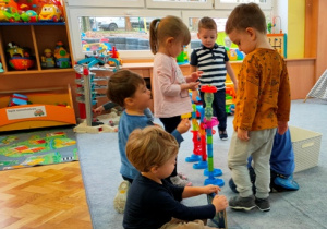 Dzieci na dywanie zbudowały przestrzenny labirynt dla szklanych kulek.
