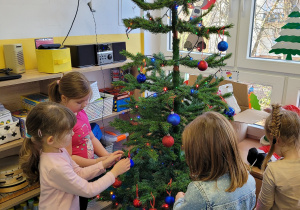 Dzieci ubierają choinkę w piękne ozdoby świąteczne.