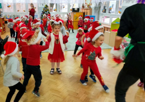 Dzieci w luźnej gromadce tańczą przy dźwiękach muzyki.