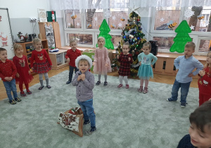 Wojtek stojąc na środku w towarzystwie dzieci śpiewa piosenkę.