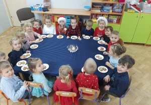 Degustacja pierniczków przez dzieci siedzących przy stole.