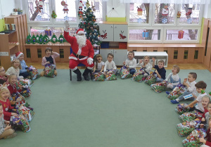 Dzieci siedzą na dywanie z Mikołajem.