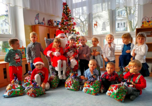 Zdjęcie grupowe- dzieci ustawione są wokół Mikołaja- w rękach trzymają prezenty.