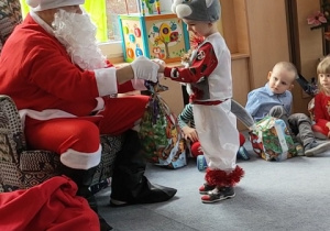 Mikołaj zaprasza do siebie kolejno dzieci i wręcza im upominki.